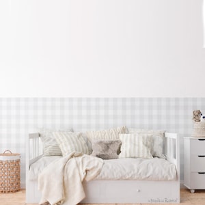 Può includere: Un divano letto bianco con diversi cuscini e una coperta color crema. Il letto è contro un muro con un motivo a scacchi grigio e bianco. Un cesto di vimini e un comò bianco sono su entrambi i lati del letto.