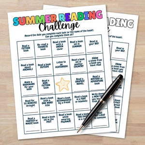 May include: Two white Summer Reading Challenge worksheets with a black pen. The worksheets have a colorful header and boxes with reading tasks. The pen is black with silver accents. The worksheets are on a light wood surface.