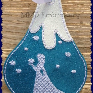 May include: A blue and white felt ornament with a white silhouette of a woman holding a flower, standing in front of a white mountain with snowflakes. The ornament has a white ribbon attached to the top and the text "MMD Embroidery" is stitched on the top of the mountain.