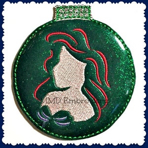 Op de afbeelding: Groene glitter kerstbal met een rood en wit geborduurd silhouet van een zeemeermin met lang golvend haar.