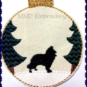 Könnte beinhalten: Ein runder, weißer, gestickter Weihnachtsbaumschmuck mit goldener Umrandung. Der Schmuck zeigt eine schwarze Silhouette eines Hundes, der vor zwei grünen Bäumen steht. Der Text "MMD Embroidery" ist auf den Schmuck gestickt.