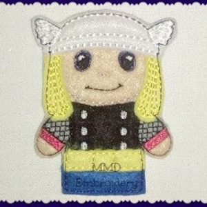 May include: A felt finger puppet of a cartoon character with blonde hair, a white helmet with horns, a black and grey shirt, red and black wristbands, and blue jeans. The puppet is smiling and has large eyes. The text "MMD Embroidery" is printed on the bottom of the puppet.