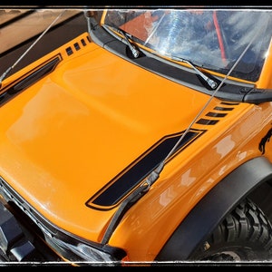 May include: Orange toy truck with black accents and a Bronco logo. The truck has a black windshield and black side mirrors.