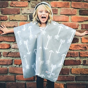 May include: A gray hooded poncho with a white arrow pattern. The poncho has a hood and a white tag with the text "My First Poncho" on the bottom right corner.