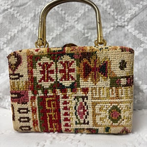 May include: A vintage handbag with a gold-tone handle. The bag features a tapestry design with a mix of red, green, yellow, and pink geometric patterns. The bag has a rectangular shape and a metal clasp.