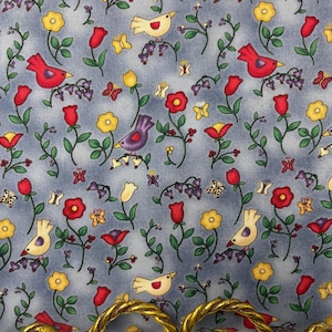 May include: A fabric with a light blue background featuring a repeating pattern of red, yellow, and purple birds, flowers, and butterflies. The fabric is accented with a gold-colored, ornate, twisted metal handle.