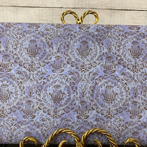 May include: A close-up of a purple fabric with a brown damask pattern. The fabric is displayed on a gold metal stand.