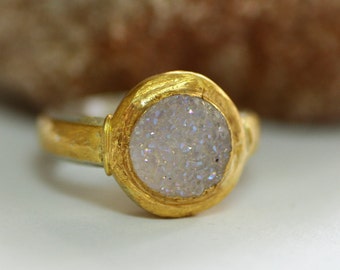 May include: A gold ring with a white, sparkly, round stone set in a bezel setting.