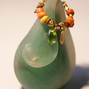 K&ouml;nnte beinhalten: Eine gr&uuml;ne Glasskulptur mit einer goldenen und korallenfarbenen Perlenkette mit einem gr&uuml;nen Edelsteinanh&auml;nger.