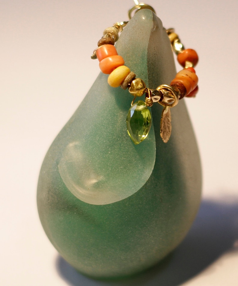 K&ouml;nnte beinhalten: Eine gr&uuml;ne Glasskulptur mit einer goldenen und korallenfarbenen Perlenkette mit einem gr&uuml;nen Edelsteinanh&auml;nger.