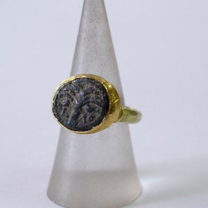 May include: A gold ring with a black oval-shaped stone set in the center. The stone has a detailed design of a face.