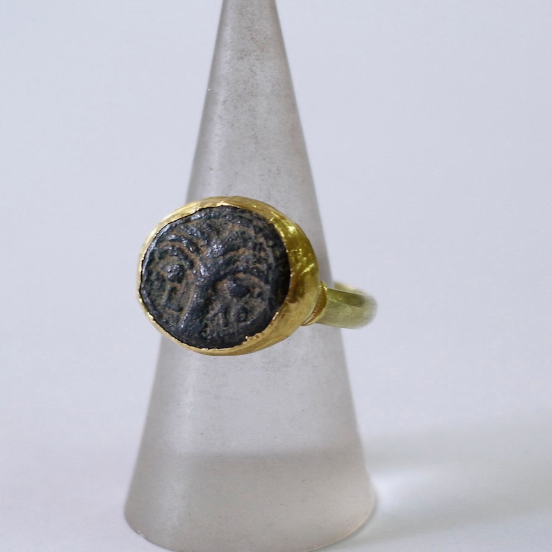 May include: A gold ring with a black oval-shaped stone set in the center. The stone has a detailed design of a face.