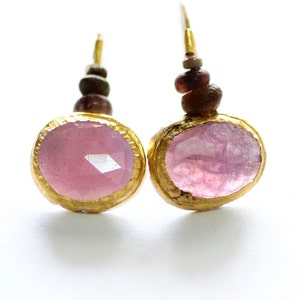May include: A pair of gold earrings with pink gemstone accents and brown beads. The earrings have a simple design and are perfect for everyday wear.