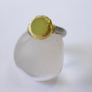 May include: A silver ring with a gold setting and a light green gemstone.