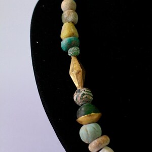 May include: A necklace made of various colored glass beads, including turquoise, green, and brown. The necklace features a gold spacer bead in the center.