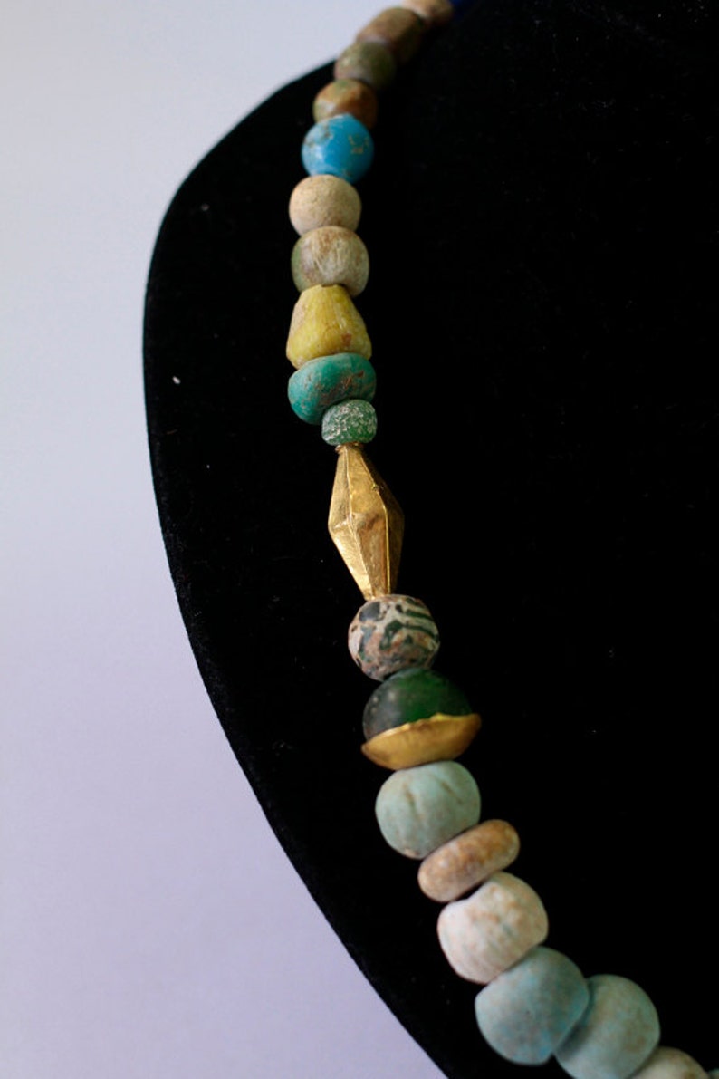 May include: A necklace made of various colored glass beads, including turquoise, green, and brown. The necklace features a gold spacer bead in the center.