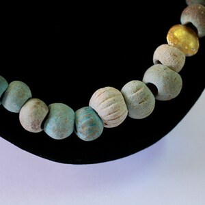 May include: A close-up of a necklace made of turquoise and gold beads. The beads are strung on a cord and are arranged in a pattern. The necklace is on a black velvet background.