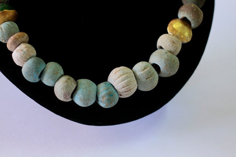 May include: A close-up of a necklace made of turquoise and gold beads. The beads are strung on a cord and are arranged in a pattern. The necklace is on a black velvet background.