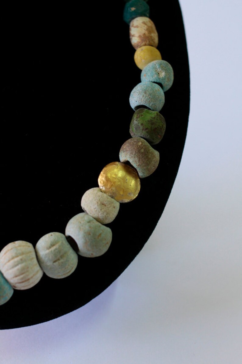 May include: A close-up of a necklace made of various colored beads, including blue, green, yellow, and gold. The beads are strung on a black cord and are arranged in a gradient pattern.