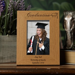 May include: A wooden picture frame with a graduation cap design and the word "Graduation" engraved on the top. The frame has a photo of a person wearing a graduation cap and gown, holding a diploma. The text below the photo reads "Amy Rutt, University of Lincoln, September 2019."