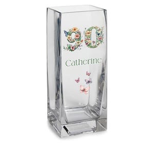 May include: Clear glass vase with a square base and a rectangular body. The vase is decorated with the number "90" in a floral design, the name "Catherine", and butterfly accents.