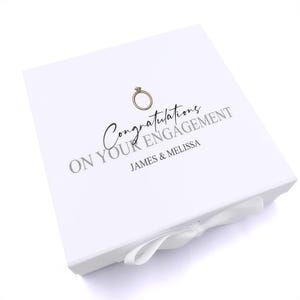 A white box with a ribbon bow, featuring a gold ring and the text "Congratulations on your engagement James & Melissa" printed on it.