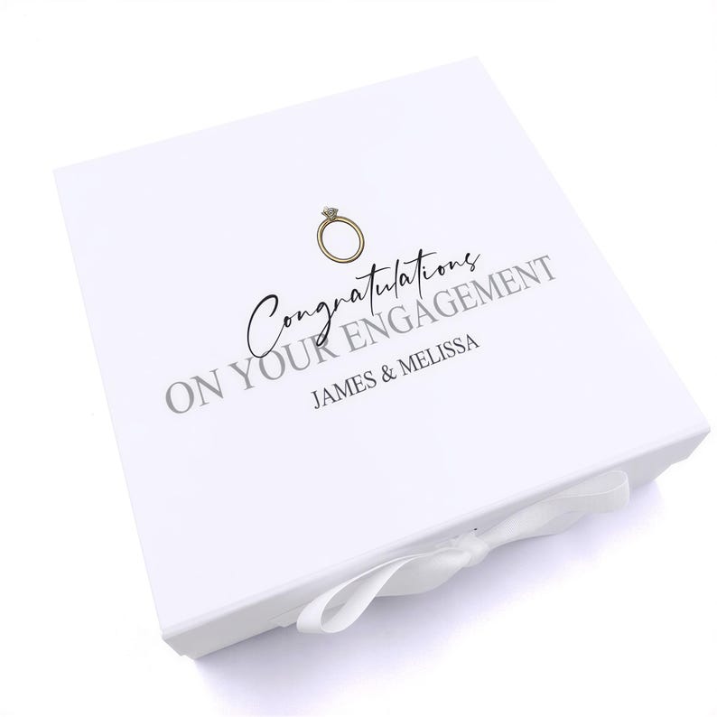A white box with a ribbon bow, featuring a gold ring and the text "Congratulations on your engagement James & Melissa" printed on it.