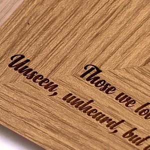a close-up view of a wooden surface with a textured, grainy appearance. The text engraved on the wood reads "Unseakable, Unheard, Unburdened".