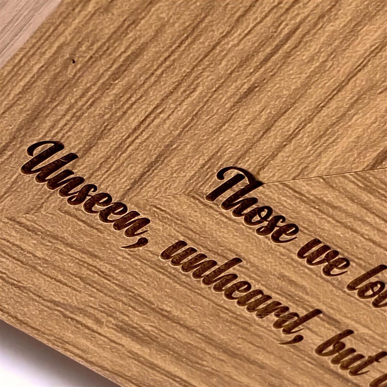 a close-up view of a wooden surface with a textured, grainy appearance. The text engraved on the wood reads "Unseakable, Unheard, Unburdened".