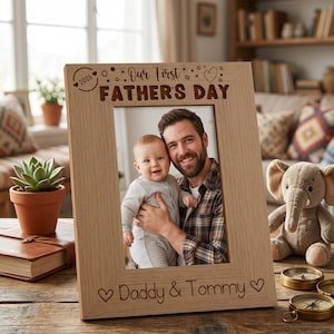 A wooden picture frame with a photo of a smiling man holding a baby, surrounded by various objects such as a potted plant, a stuffed elephant, and a book.