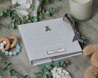 May include: A white baby memory book with a silver bear charm and the text "Sometimes the littlest things take up the most room in your heart".