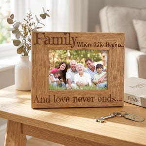 A wooden picture frame with a family photo inside, placed on a wooden table next to a key and a book.