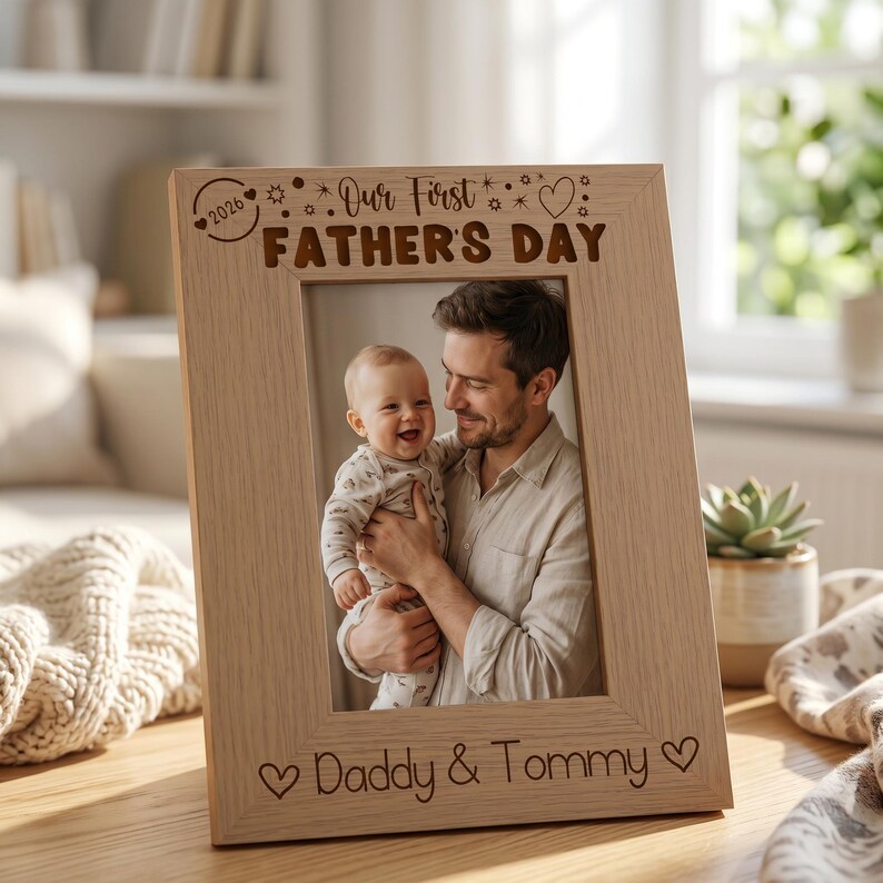 A wooden picture frame with a photo of a smiling man holding a baby, and the text "Our First Father's Day" written on the frame.