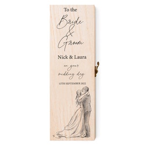 May include: A wooden box with a hinged lid, personalised with the text "To the Bride & Groom Nick & Laura on your wedding day 12TH SEPTEMBER 2022". The box features a black and white illustration of a bride and groom embracing.