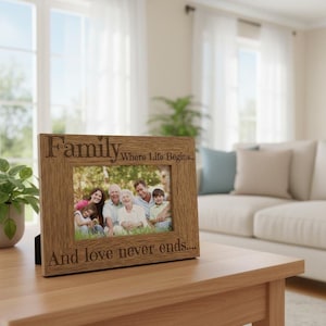 A wooden picture frame with a family photo inside sits on a wooden table in a living room, with a couch and potted plant visible in the background.