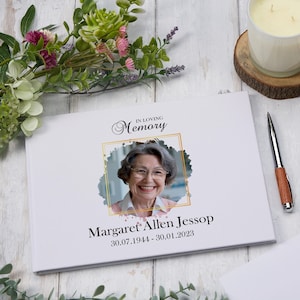 May include: White memorial book with a gold frame around a photo of a woman smiling. The text "In Loving Memory" is above the photo and the text "Margaret Allen Jessop 30.07.1944 - 30.01.2023" is below the photo.