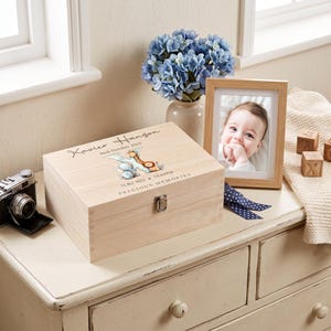A wooden box with a picture of a baby and the name "Xavier" is placed on a wooden dresser next to a framed photo of a baby.