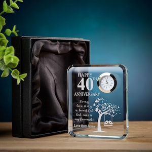 May include: A clear glass clock with a silver face and hands. The clock is engraved with the words "Happy 40th Anniversary" and a quote about love stories. The clock is sitting on a wooden surface.