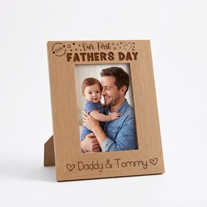 A wooden picture frame with a photo of a man holding a baby, and the text "Our First Father's Day" written on the frame.