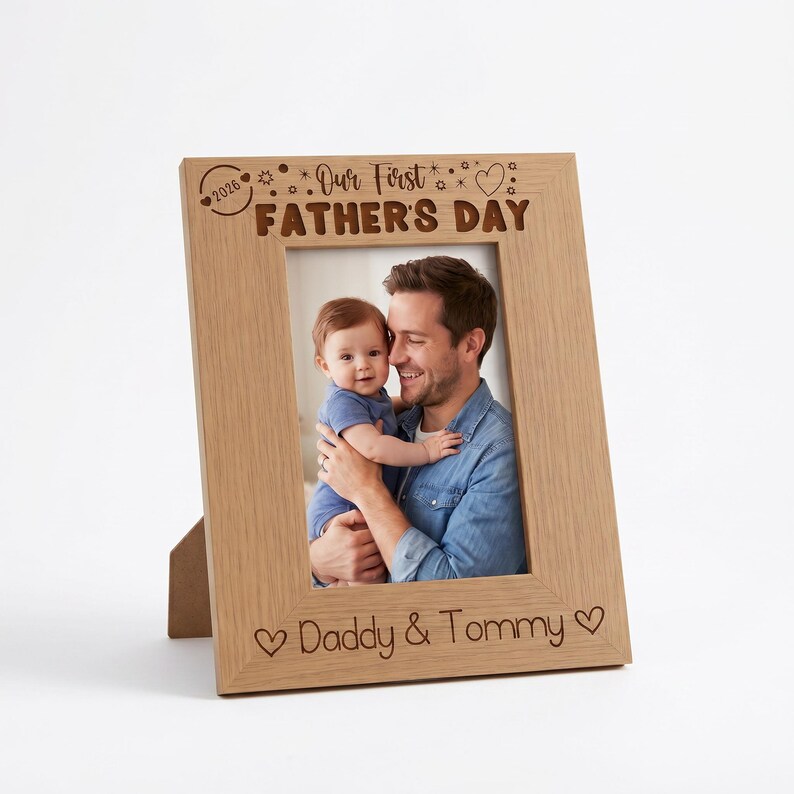 A wooden picture frame with a photo of a man holding a baby, and the text "Our First Father's Day" written on the frame.