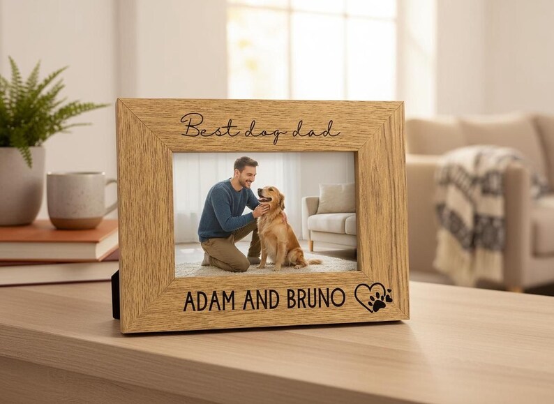 A wooden picture frame with a photo of a man and a dog inside, placed on a wooden surface. The frame has a personalized message that reads "Best day dad" and "Adam and Bruno".