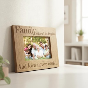 A wooden picture frame with a family photo inside, placed on a white surface. The frame has a message engraved on it that says "Family Where Life Begins... And love never ends..."