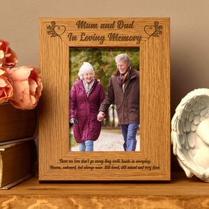 May include: A wooden photo frame with an engraved inscription that reads "Mum and Dad In Loving Memory." The frame holds a photo of an older couple walking hand-in-hand in a park. The inscription below the photo reads "Those we love don't go away they walk beside us everyday. Unseen, unheard, but always near. Still loved, still missed and very dear."