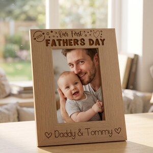 A wooden picture frame with a photo of a smiling man holding a baby, and the text "Our First Father's Day" written on the frame.