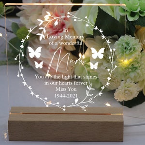 K&ouml;nnte beinhalten: Ein wei&szlig;es, beleuchtetes Acrylschild mit einem Blumengirlanden und Schmetterlingen. Das Schild tr&auml;gt die Aufschrift "In Loving Memory of a wonderful Mum You are the light that shines in our hearts forever Miss You 1944-2021".