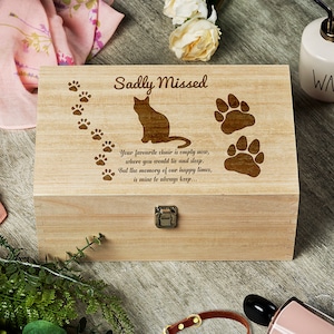 May include: A wooden box with a cat silhouette and paw prints engraved on the lid. The box has a hinged lid and a metal latch. The text "Sadly Missed" is engraved on the lid, along with a poem about remembering a pet.