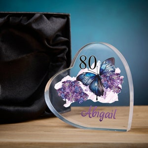 May include: A clear heart-shaped acrylic paperweight with a blue butterfly and purple flowers. The number 80 is printed on the paperweight, along with the name Abigail.