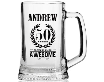 May include: A clear glass beer mug with a black design that says "Andrew 50 Years of Being Awesome" with a laurel wreath around the number 50.