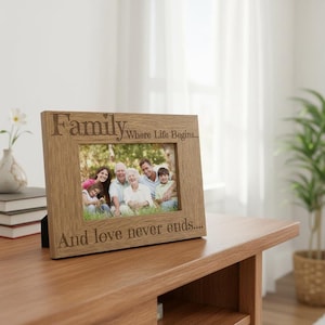 A wooden picture frame with a family photo inside, placed on a wooden table. The frame has a message engraved on it that says "Family Where life begins... And love never ends..."