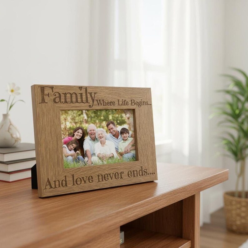 A wooden picture frame with a family photo inside, placed on a wooden table. The frame has a message engraved on it that says "Family Where life begins... And love never ends..."
